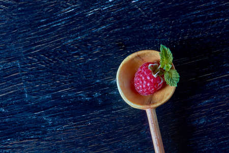 Raspberries in a wooden spoon on black background