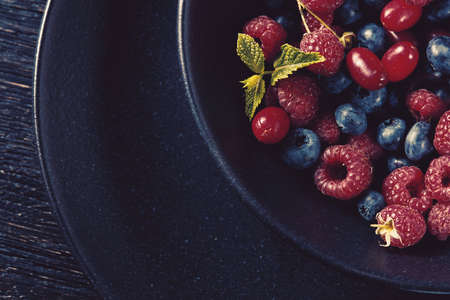 Close up of black bowl full with fresh organic berries and mint on black wood backgroundの写真素材