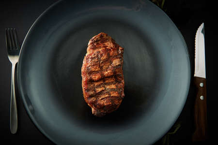 Beef steak served on black plate with fork and knife on dark tableの写真素材