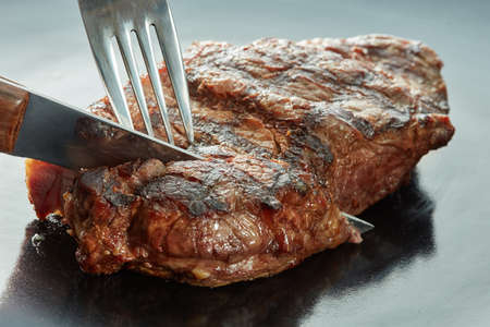 piece of steak cut with a fork and knife on dark background