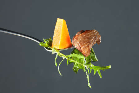 baked pumpkin, piece of duck meat and arugula on a fork. Isolated on blackの写真素材