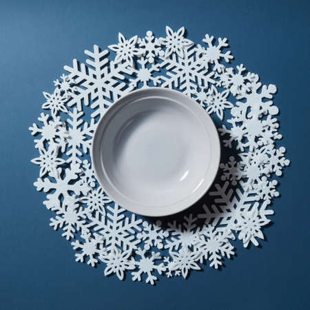 Frame from snowflakes with white bowl in the center on a blue background. Space for textの写真素材