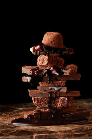 mountain of pieces of dark chocolate with drops of chocolate on a marble background