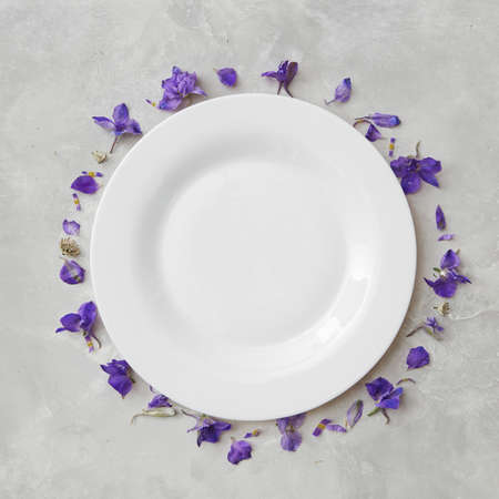 Round frame of flowers and a white plate on a light background, copy space flat layの写真素材