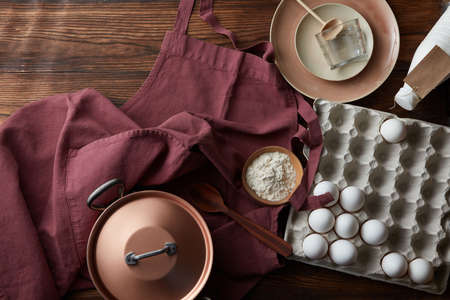 Kitchen utensils and ingredients for making a pie on an old wooden table with an apron.