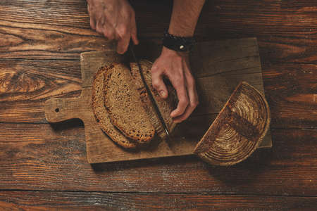 Dark bread on a wooden brown board. A man cuts bread flat layの写真素材
