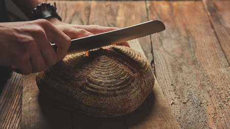 Hands of a man cutting fresh rye bread on a wooden backgroundの写真素材