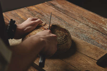 Man baker cutting a knife bread on a wooden cutting board on old wooden backgroundの写真素材