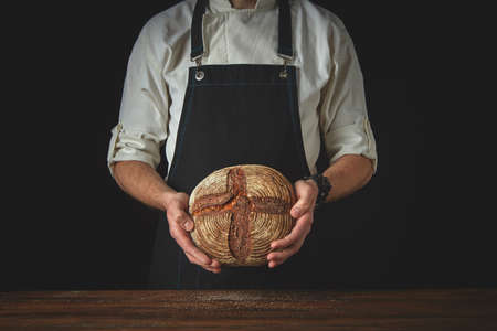 baker in an apron holds bread in hands on a black backgroundの写真素材
