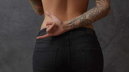 Beautiful woman body on a dark background. Nude woman back with tattoos on her hands showing Sign of the hornsの写真素材