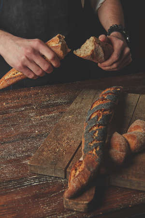 Men's hands hold divided baguette halves on a dark wooden background