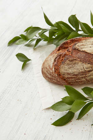 Rye organic bread with branches of leaves on a white tableの写真素材