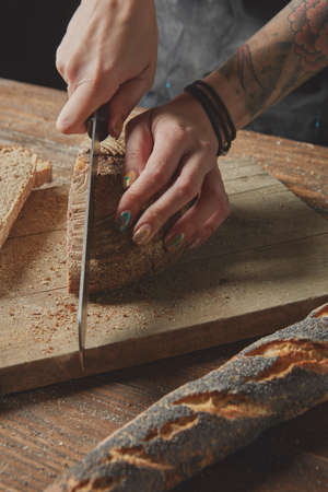 Woman's hands cut fresh bread on a wooden boardの写真素材