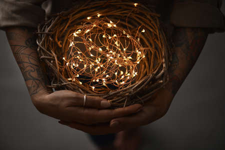 wreath of twigs and Christmas lights in female hands on a dark background flat layの写真素材