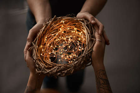 natural wreath made from twigs, decorated with Christmas garland, two women holding a wreath on a dark backgroundの写真素材