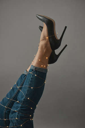 The legs of the woman are stretched high in a vertical form and decorated with a festive Christmas garland on a gray background.の写真素材