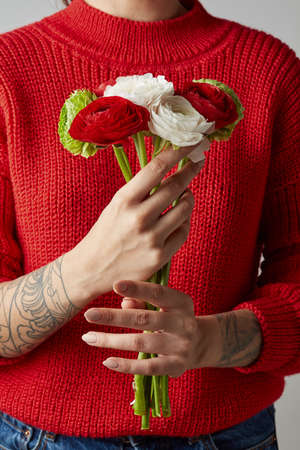 girl with a tattoo on her hands in a red knitted sweater holds a bouquet of flowers. a happy Valentine's dayの写真素材
