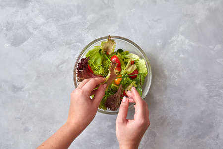 woman is preparing a salad of fresh vegetables on a gray background. Step-by-step recipe, a cooking...