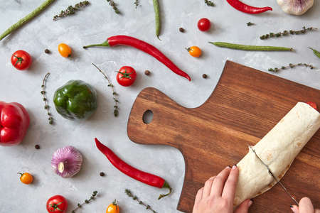 The girl cuts the finished burrito on a wooden board. Photo of a step-by-step cooking burrito. Top view, flat lay.の写真素材