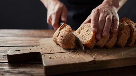 man cutting fresh bread on wooden tableの写真素材