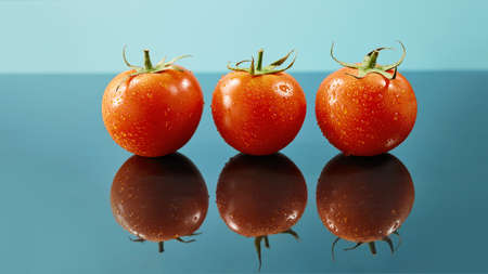 shot of red tomatoes surface with water drops isolated on glossy blue backgroundの写真素材