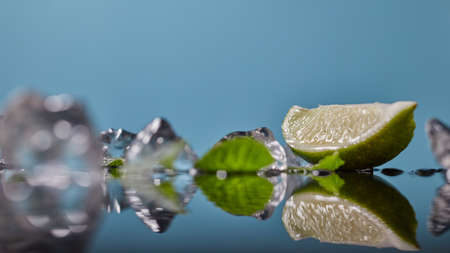 Slice of lime wedge, ice and mint isolated on blue backgroundの写真素材
