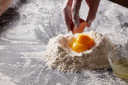A woman holds an egg shell against a background of flour with yolks. Preparation of the doughの写真素材