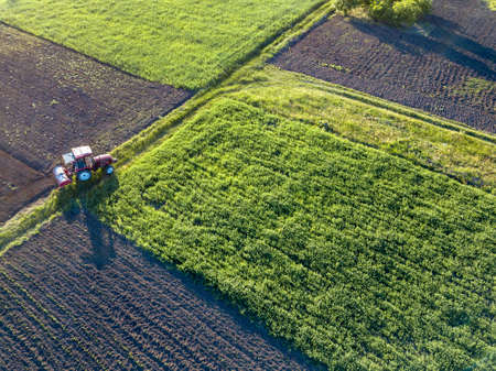 Aerial view from the drone, a birds eye view of agricultural fields with a road through and a tractor on it, in the evening, at sunsetの写真素材
