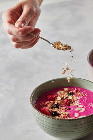 A female hand prepares a useful smoothie with berries and granola
