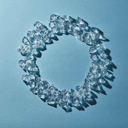 Cubes of cold ice in the form of a round frame on a blue background. Flat lay
