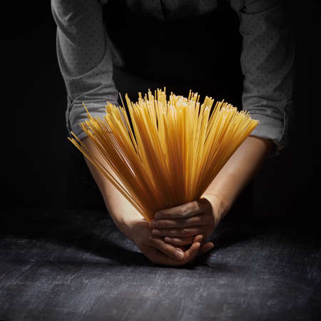 Womans hands holding Raw spaghetti in dark backgroundの写真素材