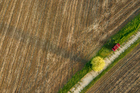 Aerial view from the drone, a birds eye view of agricultural fields with a road through and red car on it in the spring evening at sunsetの写真素材