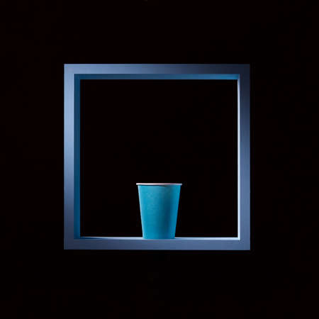 Blue paper cup in a blue square frame on a black square background. Symmetrical central composition.の写真素材