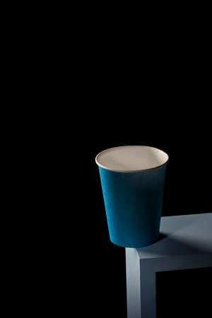 A blue paper cup stands on the edge of a blue square frame on a black square background.の写真素材