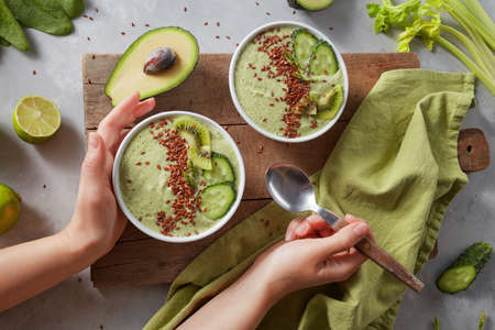 green smoothie bowl with fresh kiwi, flaxseeds, cucumber and avocado in the female handsの写真素材