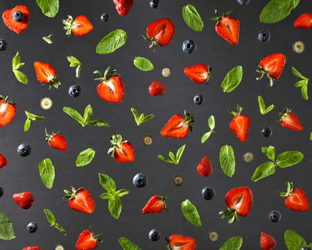 Flat lay view on fruit pattern with strawberries, blueberries and mint leaves on a black background.の写真素材
