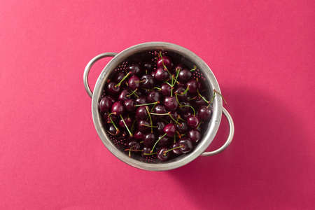 Summer ripe sweet cherry berries in a colander on a red paper background. Top view.の写真素材