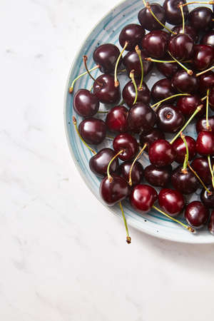 Freshly picked cherries on a half of blue plate on gray concrete background. Colorful organic...