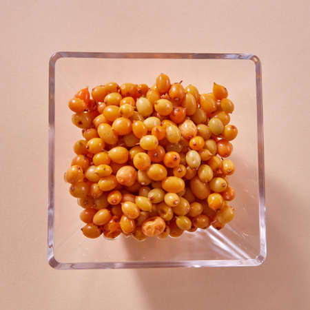 Natural organic sea buckthorn in the glass plate - yellow ripe sweet berries on a beige paper...