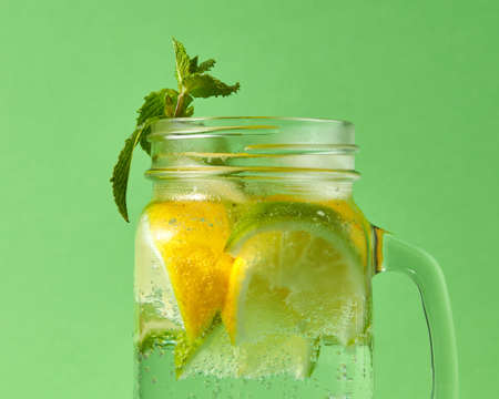 A close-up of green mint and natural citrus fruit-slices of lemon and lime, cubes of ice in a glass...