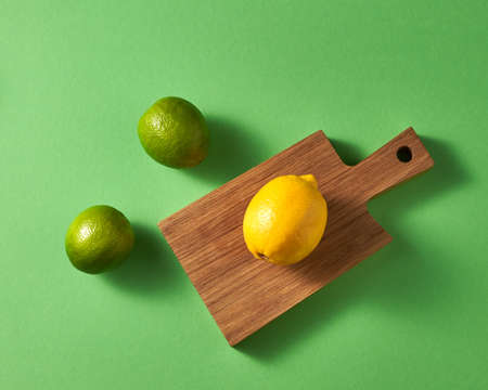 Ripe bright green limes and one yellow lemon on a wooden board on a green background.の写真素材