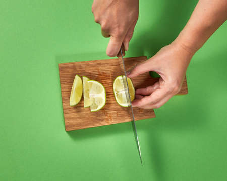 Slices of natural organic green lime, cutting by woman hands on a wooden cutting board on green.の写真素材