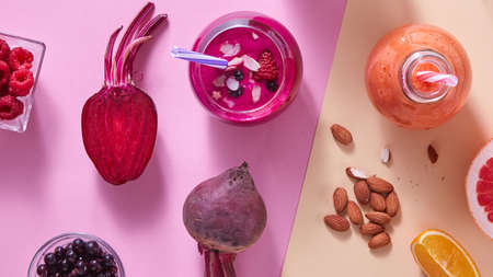 two glasses of colorful smoothies with vegetables, berries, nuts and drinking straw on a colored paper backgroundの写真素材