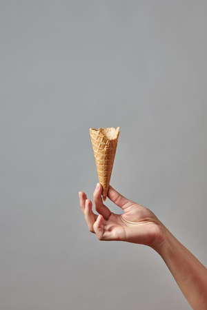 A womans hand holds an empty waffle cone on a gray backgroundの写真素材