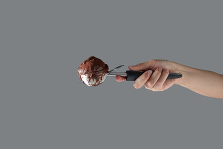 A female hand holds delicious dairy dessert cold chocolate in a metal spoon for ice cream on a gray background. Summer concept with space for text.の写真素材