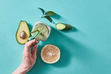 Womens fingers holding ta glass with green smoothie from green vegetables and fruits on a green...