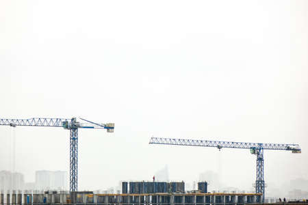 Industrial landscape with silhouettes of cranes on the gray cloudy background. Photo from the drone.