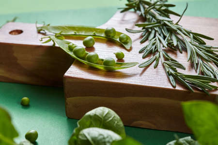 Green organic clean vegetables - rosemary, pods of peas beans, spinach on a cutting wooden board on...