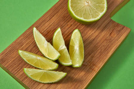 Juicy slices and half of ripe green lime on a wooden board on a green background. Healthy food...