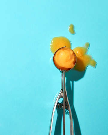 Flat lay of a spoon for ice cream with yellow mango dessert and melted ice cream on a blue background with hard shadowsの写真素材